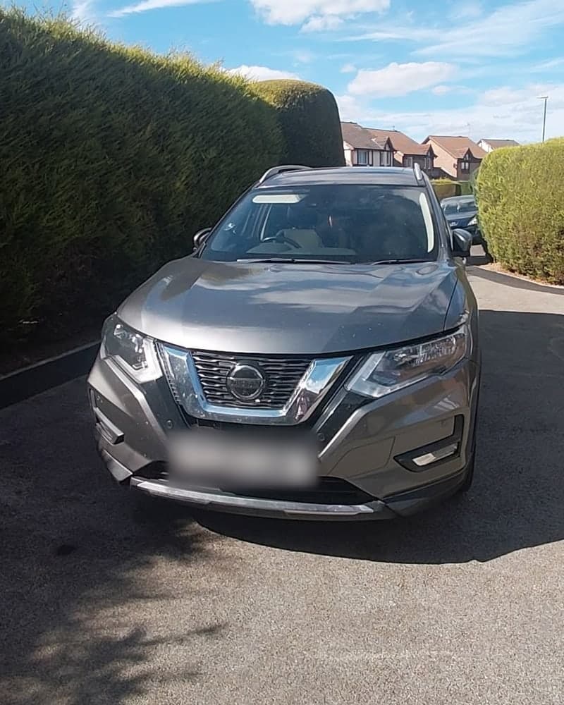 Front of a grey Nissan X-Trail after its clean, parked on a driveway between tall hedges